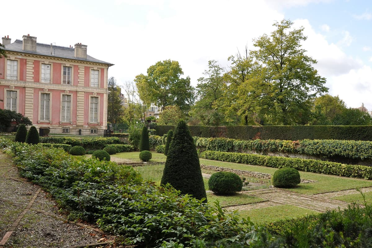 Le jardin de la Folie Saint-James : parterres taillés et ifs en cône devant un pavillon de façade rose à hautes fenêtres.